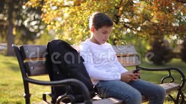 放学后男孩在公园里用电话。 十几岁的男孩在外面使用智能手机。 金秋